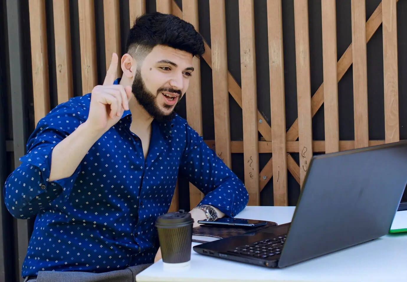 Lächelnder männlicher Geschäftsmann, der während einer Online-Konferenz mit dem Zeigefinger gestikuliert.